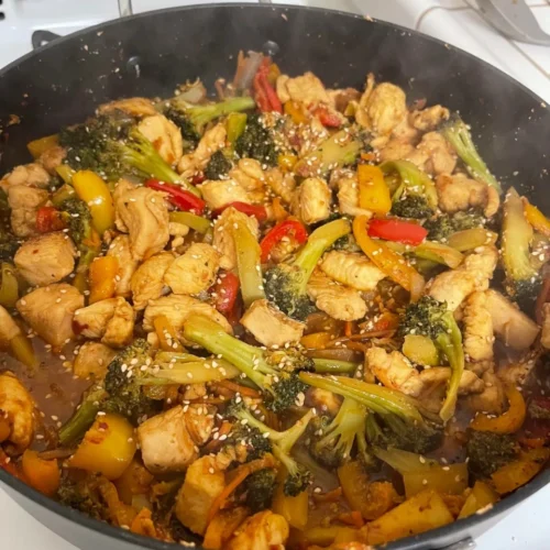 Colorful keto stir fry made with chicken, bell peppers, broccoli, and sesame seeds in a cast-iron skillet.